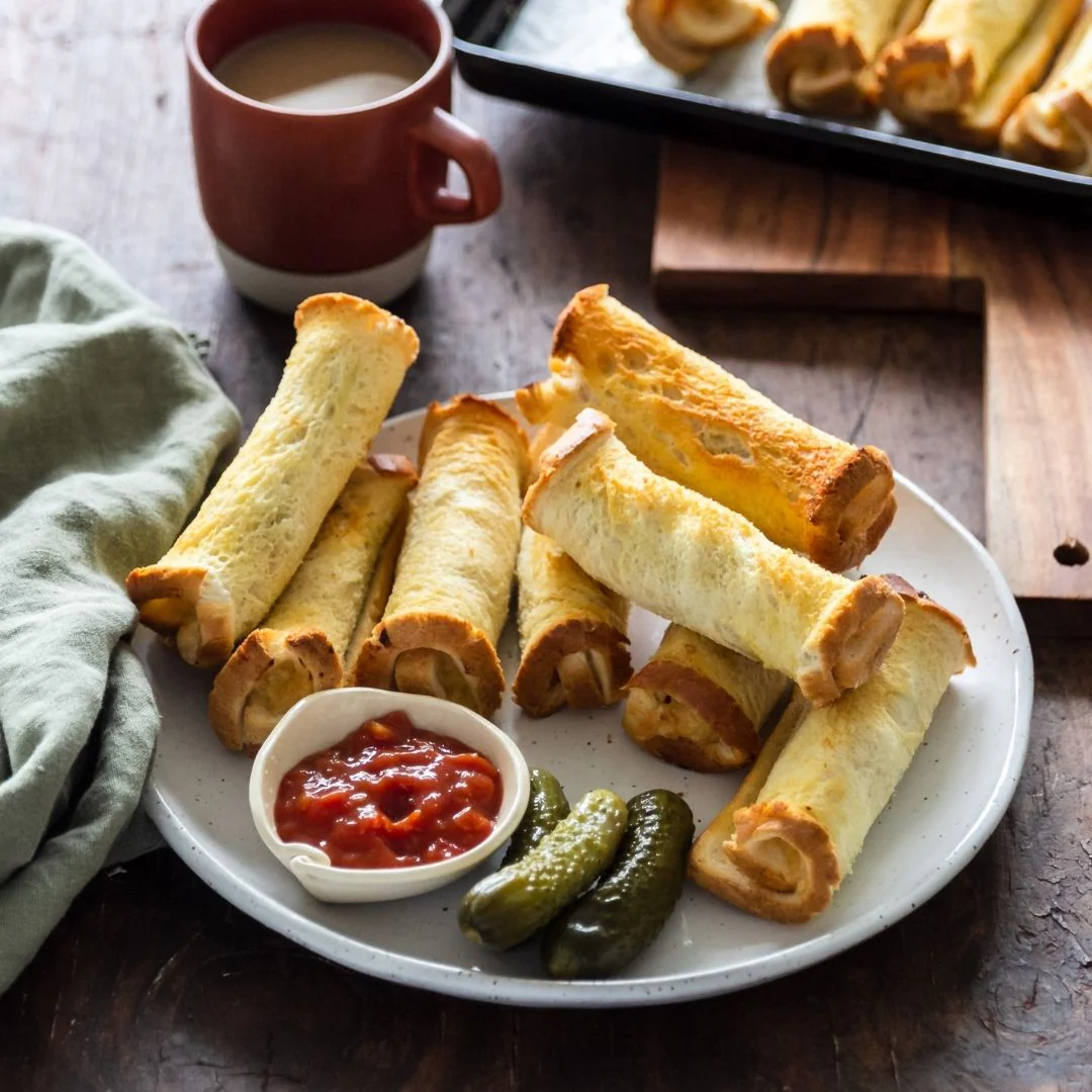 Platter of taquitos with a side of salsa and pickles on a wooden table.